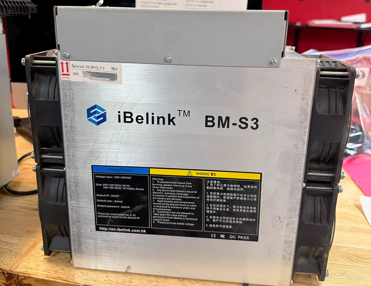 iBeLink BM-S3 miner on a workbench, with the BM-S3 panel marking and the P/N BM-S3_V1.0 TD-1 label above it