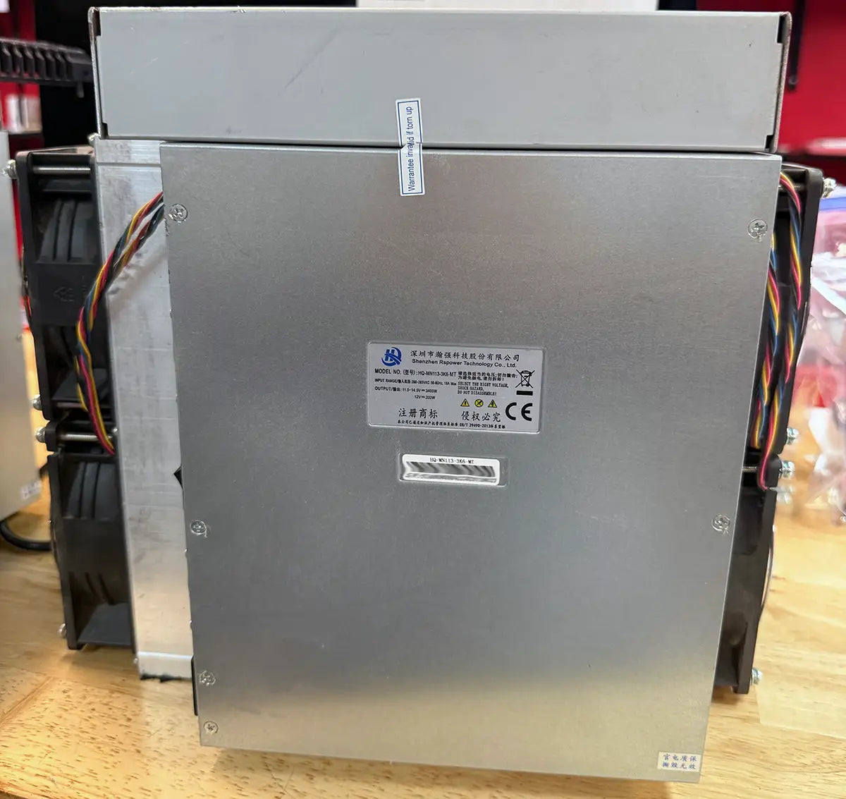 Power supply side of an iBeLink BM-S3 miner, with the factory warranty seal across the cover seam